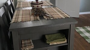 Una mesa de comedor con mantel a cuadros, un centro de mesa decorativo y un posavasos a cuadros. Hay sillas en un lado y una puerta al fondo.