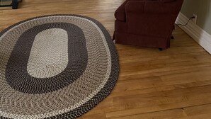 Una sala de estar con piso de madera, un sillón rojo, una lámpara y un tapete tejido grande.