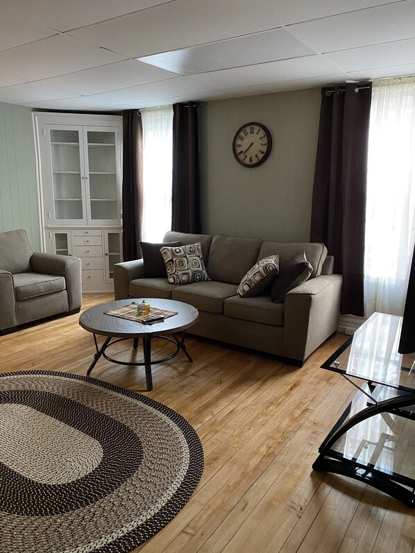 A living room with a sofa, a coffee table, a cabinet, and a clock on the wall. - On The St. Lawrence River & in Downtown Alexandria Bay! (Alexandria Bay)