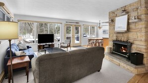 Una sala de estar con chimenea, televisor y comedor con vistas al exterior.