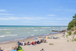 A beach with people relaxing on chairs and umbrellas, a lighthouse in the distance, and a rocky shoreline. - Grand Bend Beach House (Grand Bend)