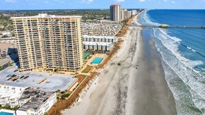 A coastal hotel with multiple high-rise buildings, a beach, and a pier.