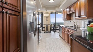 A modern kitchen with wooden cabinets, a stainless steel refrigerator, and a view of the ocean through large windows.