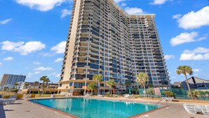 A high-rise hotel with a swimming pool and palm trees.