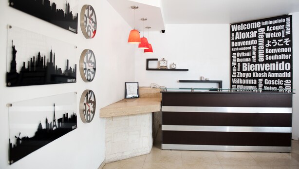 A reception area with a modern design, featuring a reception desk, a clock, and wall art depicting cityscapes.