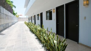 A clean, modern building exterior with a row of black doors, a tiled walkway, and a low wall with greenery.