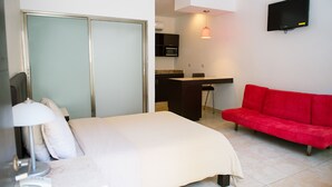 A hotel room with a bed, a desk, a red sofa, a TV, and a sliding door.