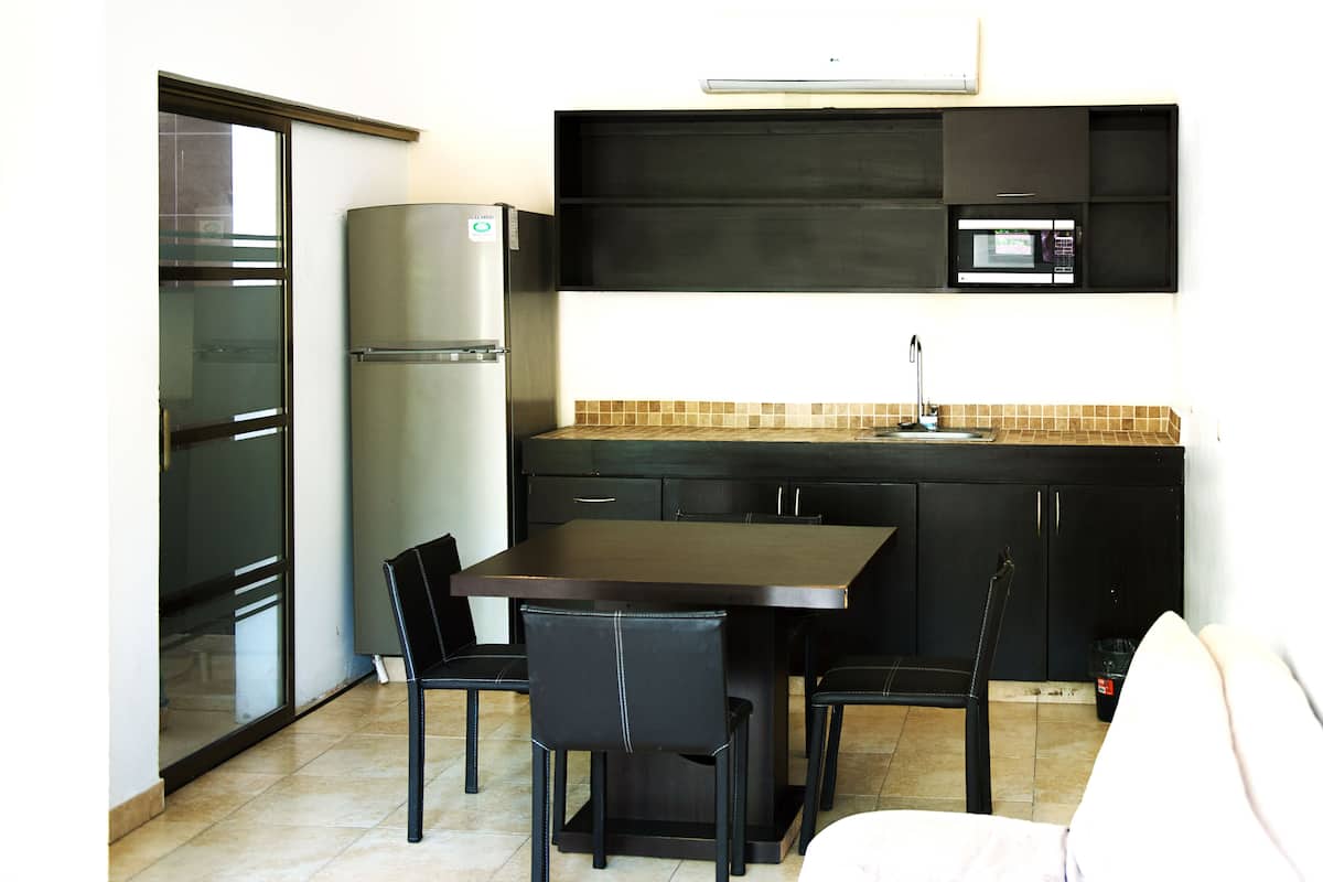 A compact kitchen with a refrigerator, microwave, and a dining table with chairs.