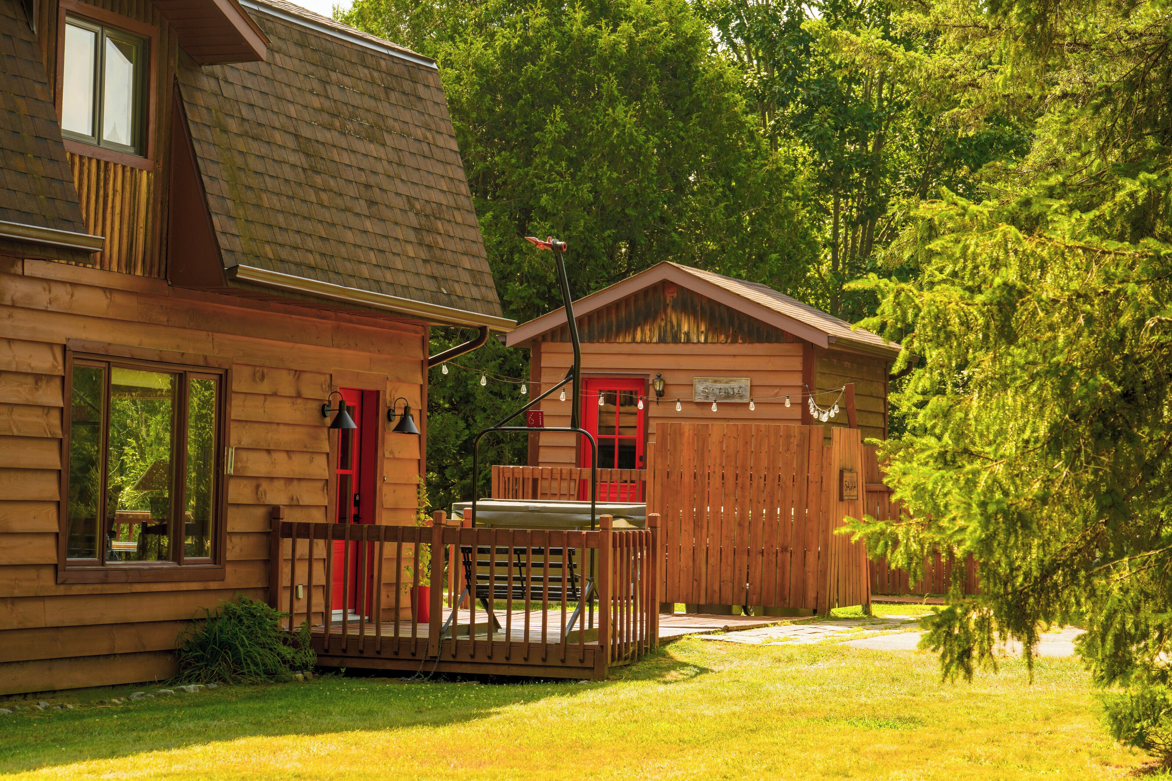 A wooden cabin with a red door, a small porch, and a fenced yard.