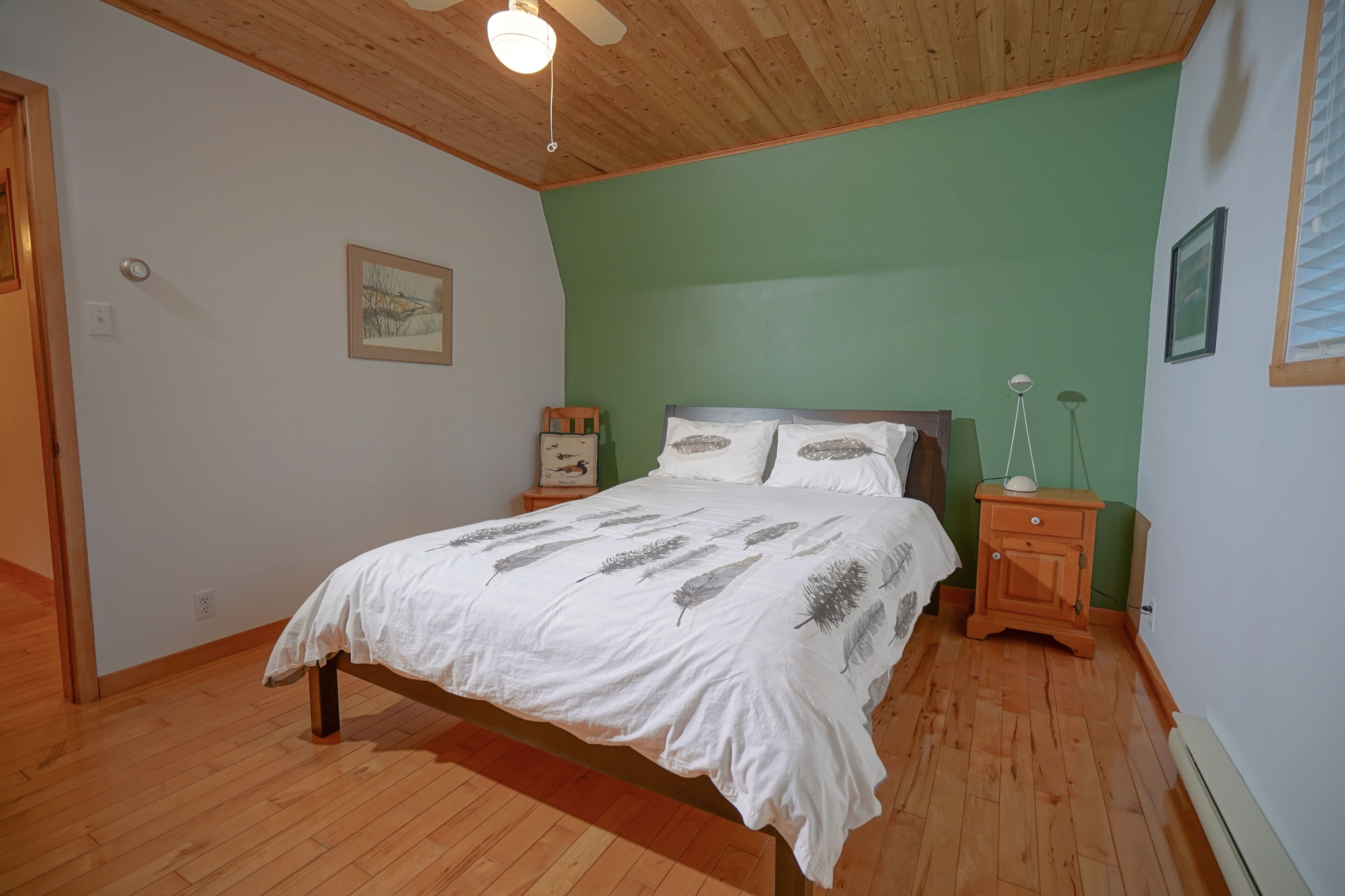 A bedroom with a wooden bed, green walls, and a ceiling fan.