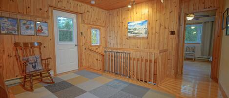 A wooden interior with a checkered floor, a rocking chair, a door, and a painting on the wall.