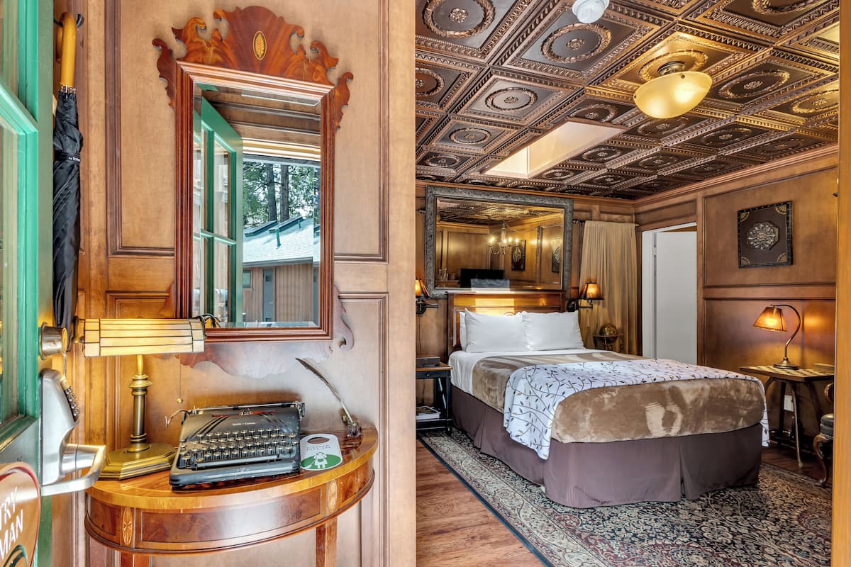 A hotel room with a large bed, a desk with a typewriter, a mirror, and a ceiling with intricate designs.