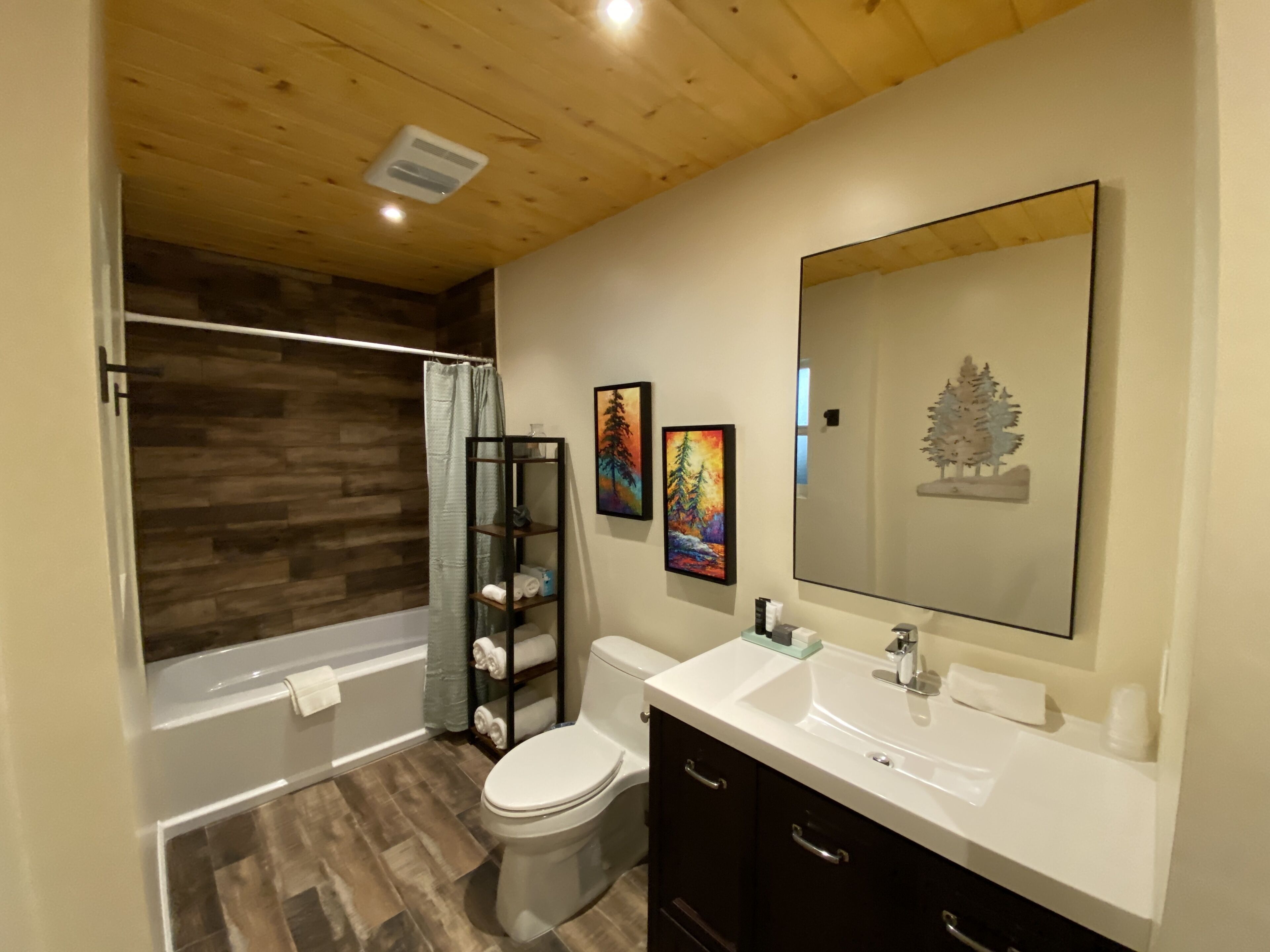 Un baño moderno con techo de madera, una bañera, un inodoro y un tocador con un espejo grande.