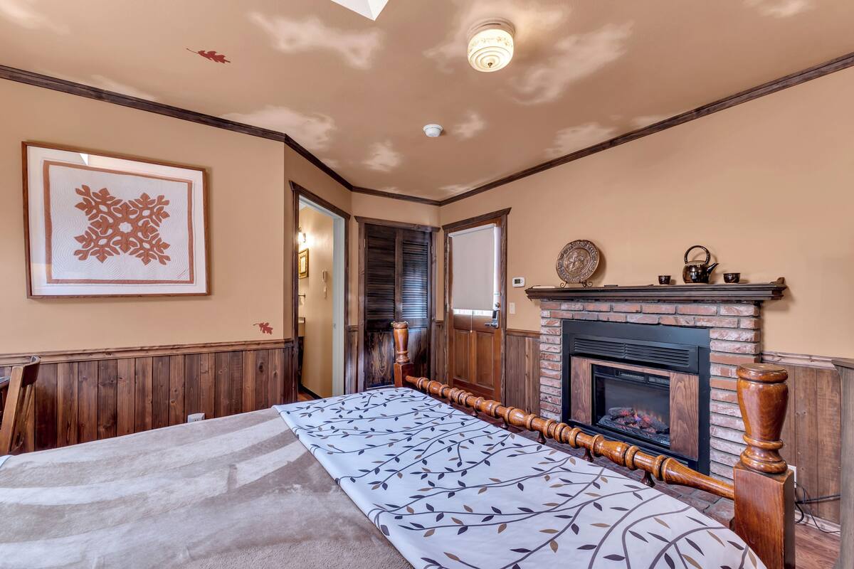 A spacious bedroom with a large bed, a fireplace, and a framed artwork on the wall.