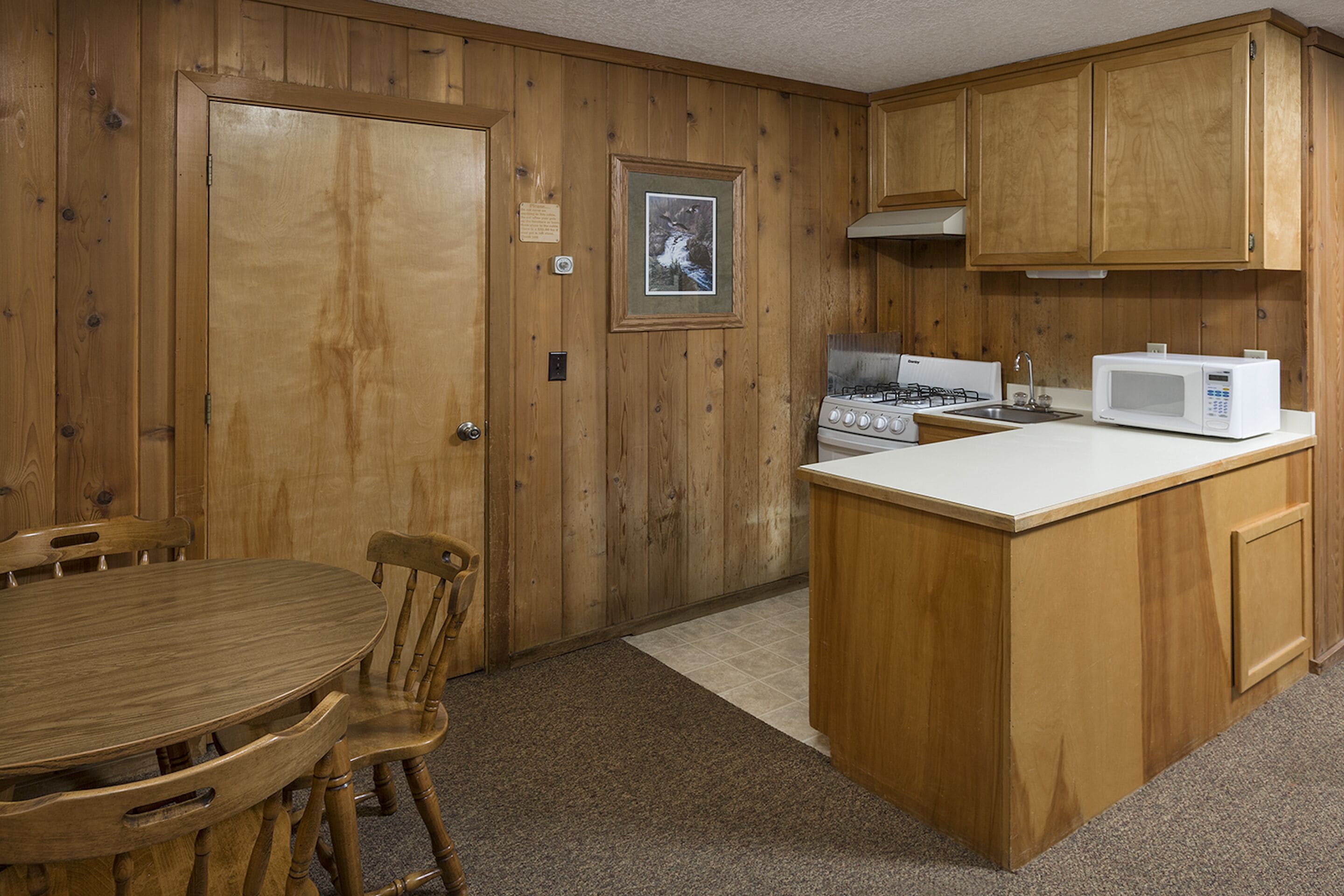 A kitchen with wooden cabinets, a gas stove, a microwave, and a dining area with a table and chairs.
