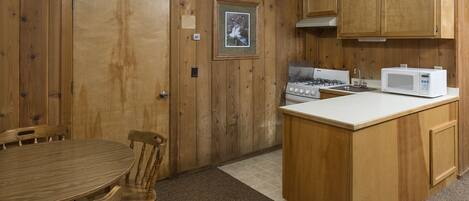 A kitchen with wooden cabinets, a gas stove, a microwave, and a dining area with a table and chairs.