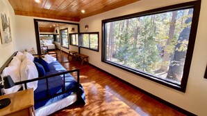 Ein Zimmer mit Bett, Holzboden, großen Fenstern und Blick auf einen Wald.