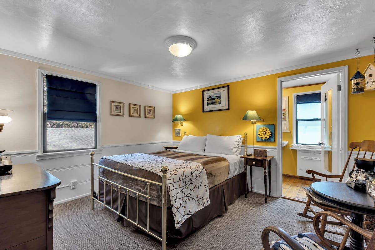 A bedroom with a bed, bedside tables, a chair, a desk, and a window with blinds.