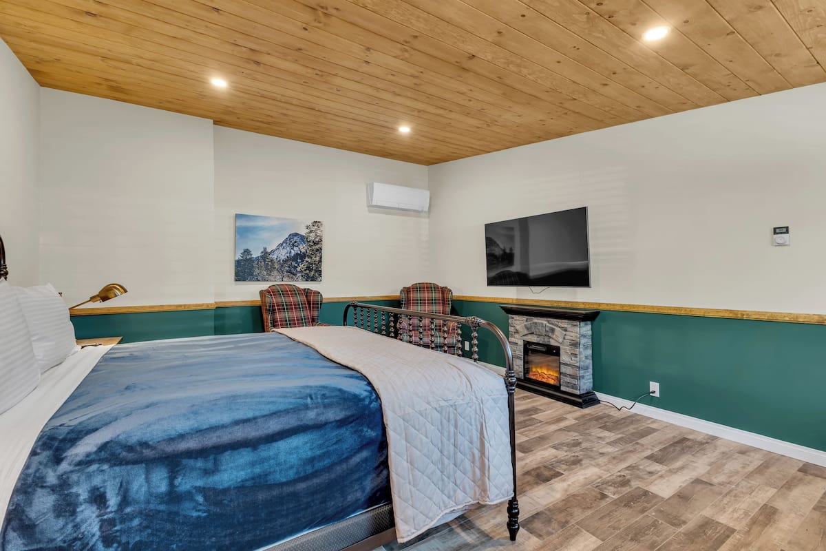 A bedroom with a bed, a fireplace, a mounted TV, and a painting on the wall.