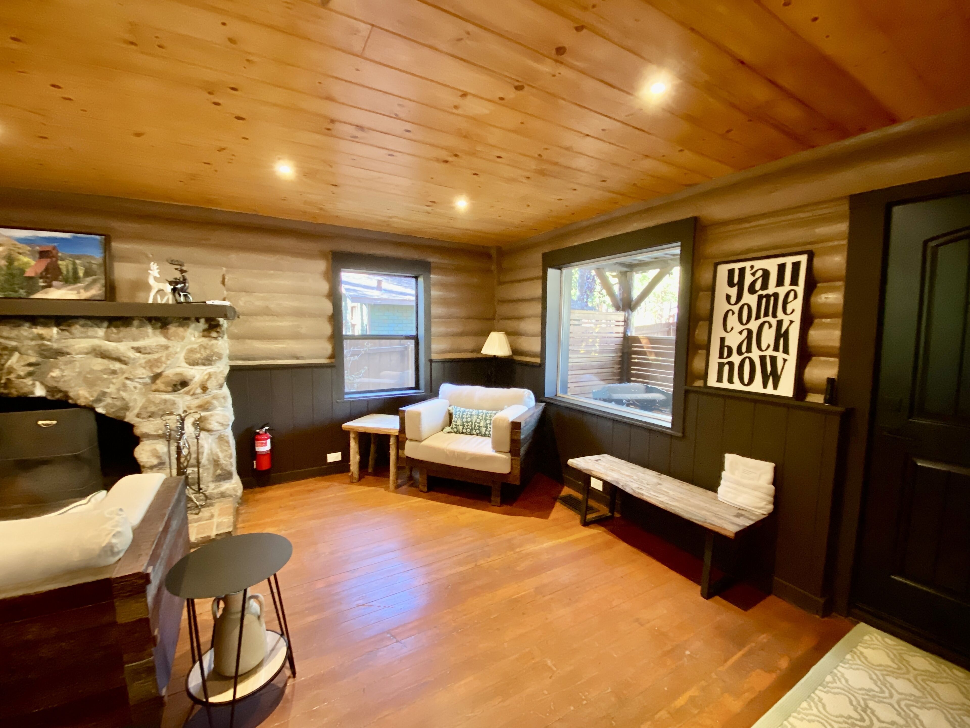 L’intérieur d’un chalet accueillant, avec une cheminée en pierre, un plancher en bois, un canapé, une petite table et un banc.