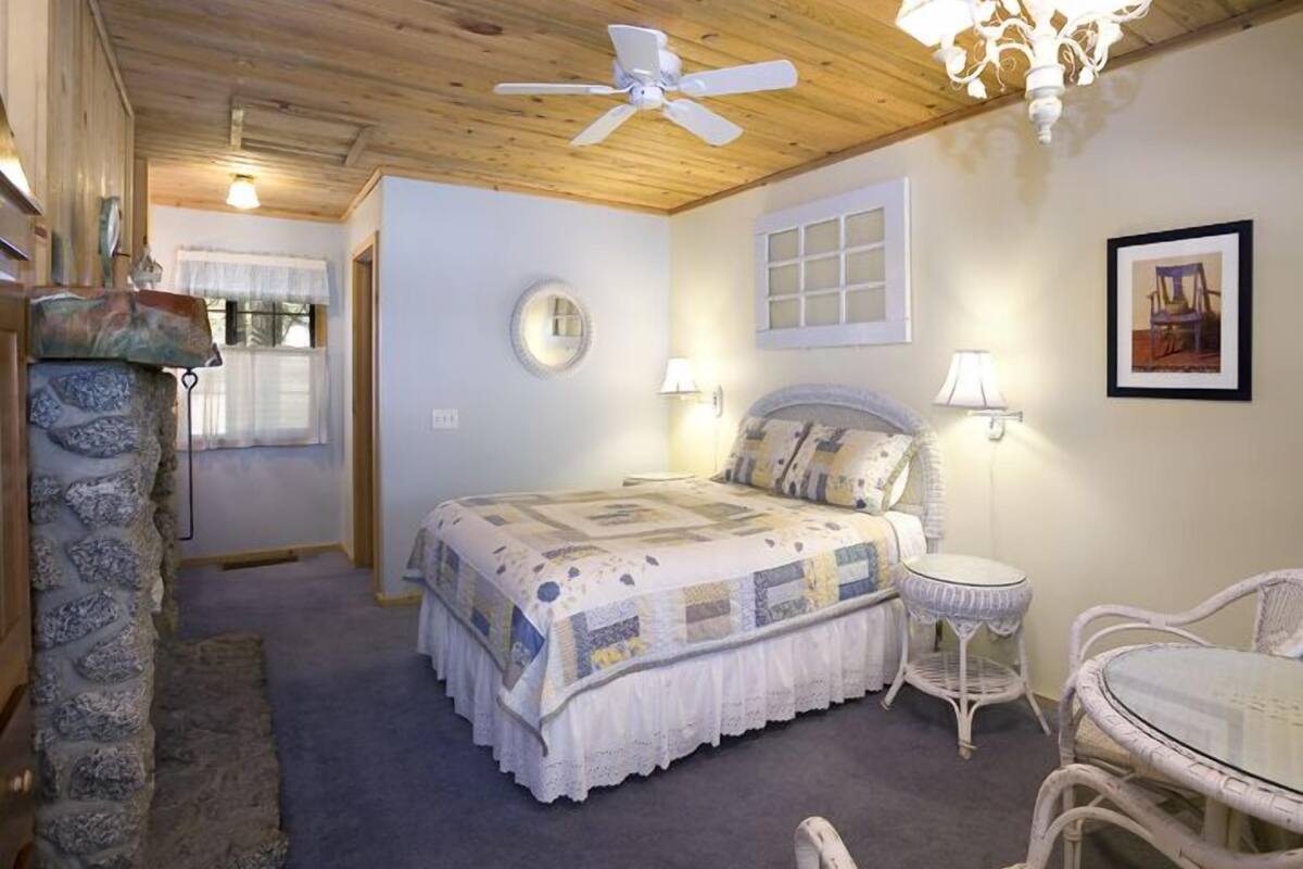 A bedroom with a bed, bedside tables, a chair, a round mirror, and a chandelier.
