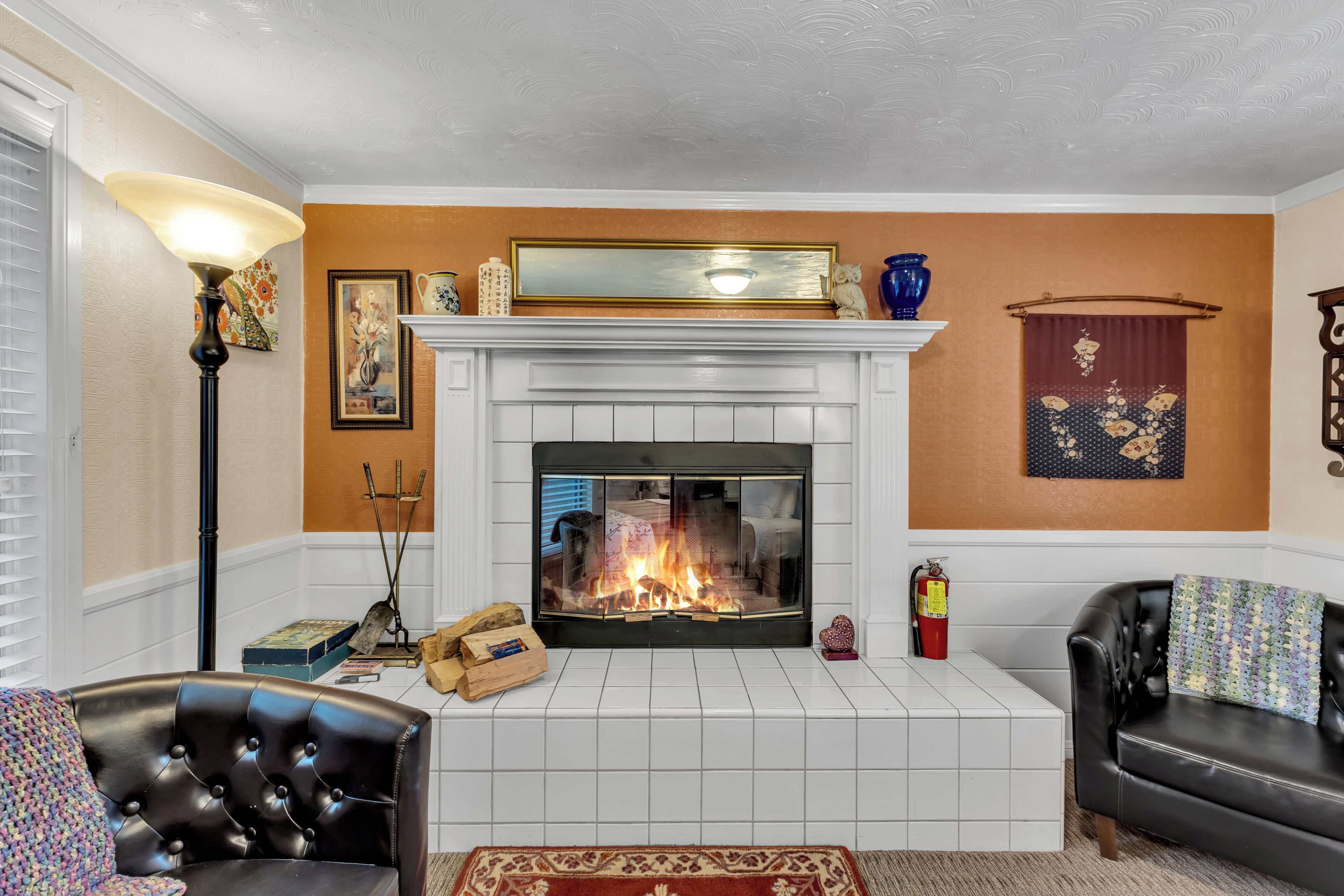 Una sala de estar con chimenea, un sofá de cuero negro, un revestimiento de chimenea de baldosas blancas y un tapete estampado.