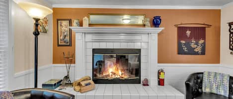 Una sala de estar con chimenea, un sofá de cuero negro, un revestimiento de chimenea de baldosas blancas y un tapete estampado.