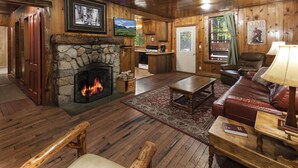 Ein gemütliches Blockhaus-Interieur mit Kamin aus Stein, Holzböden, einer Ledersofa und einem Essbereich.