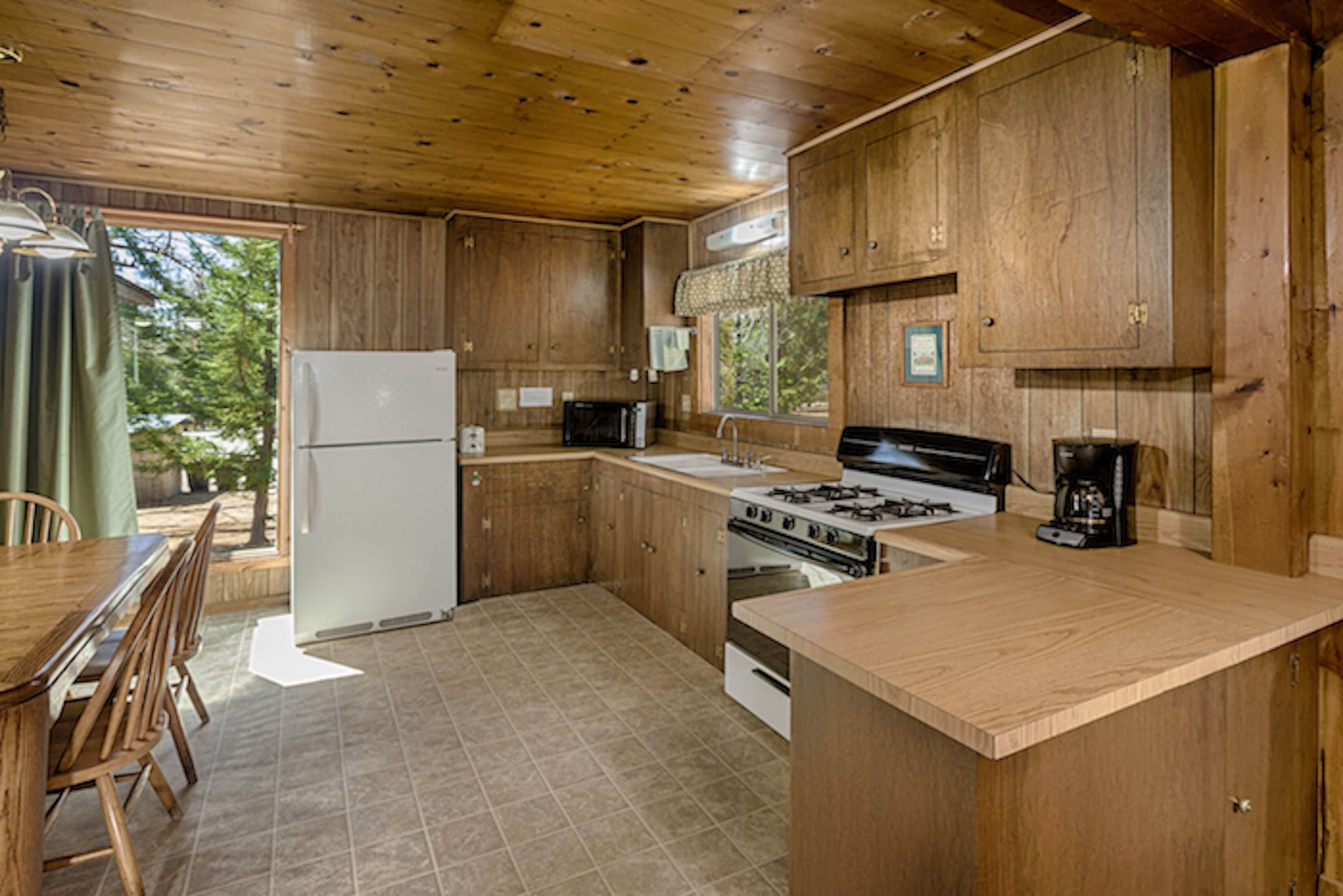 A kitchen with wooden cabinets, a refrigerator, stove, microwave, and a dining table with chairs.