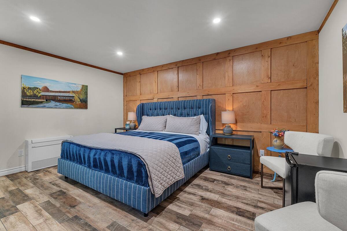 A bedroom with a large bed, wooden panel wall, bedside tables with lamps, and a painting on the wall.