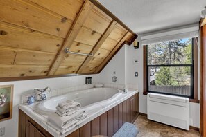 A bathroom with a wooden ceiling, a bathtub, a window with a view of trees, and a radiator.