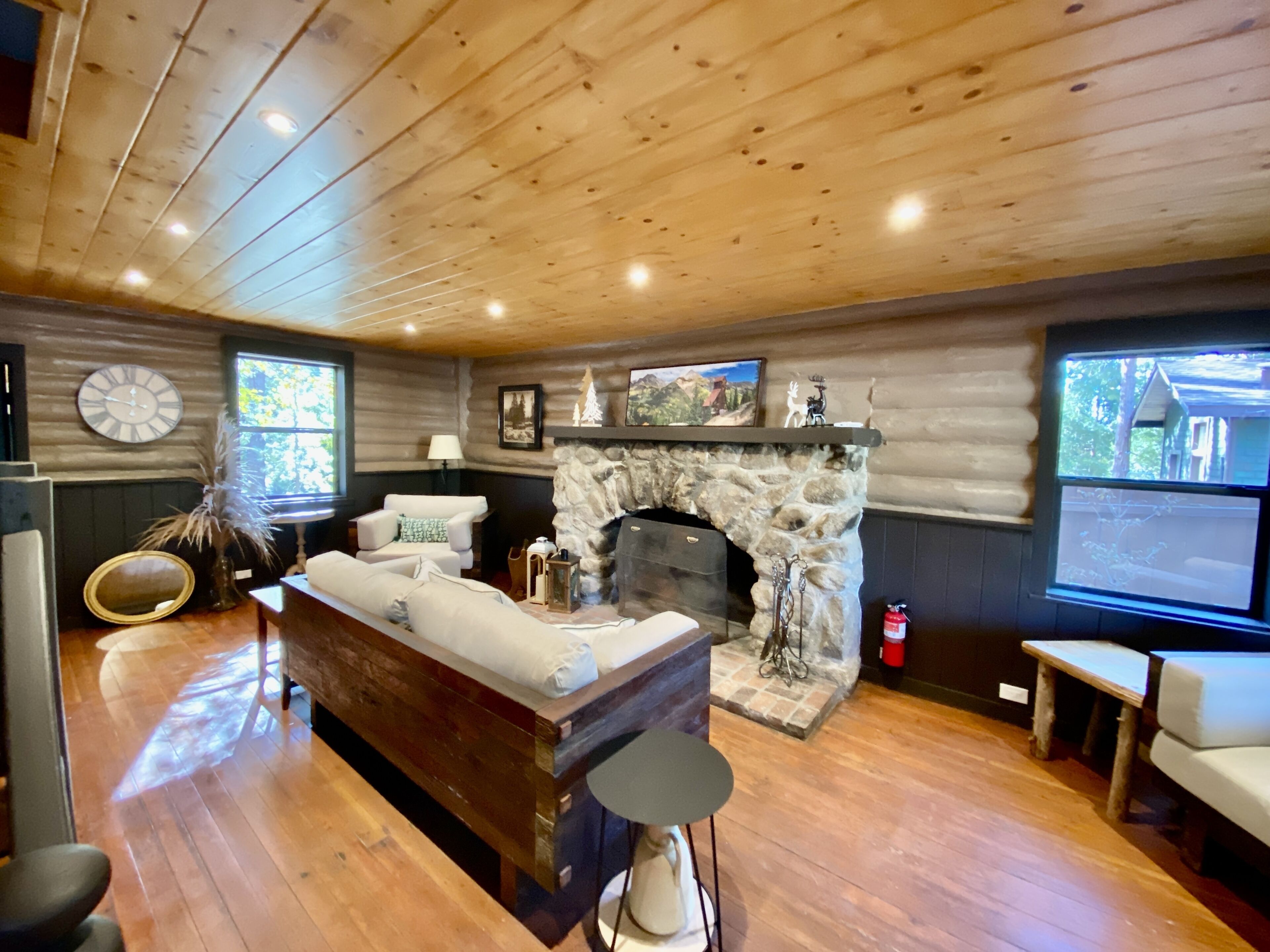 A cozy cabin interior with a stone fireplace, wooden floors, a sofa, and a television.