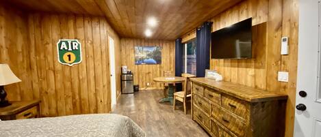 Una habitación de madera con una cama, un escritorio, un refrigerador, un televisor y un letrero que dice "AIR 1".