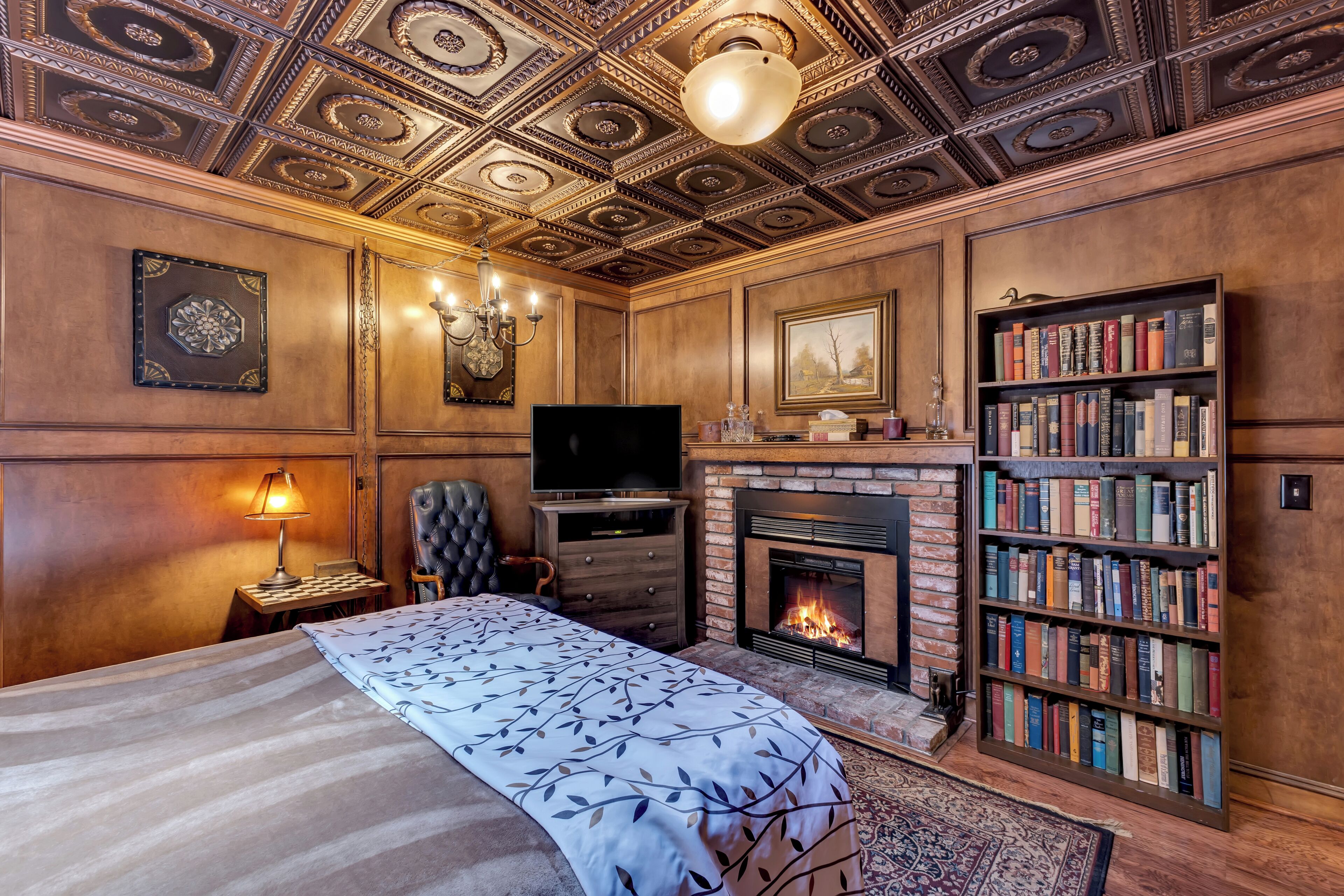 A room with a bed, a fireplace, a bookshelf, and a television.