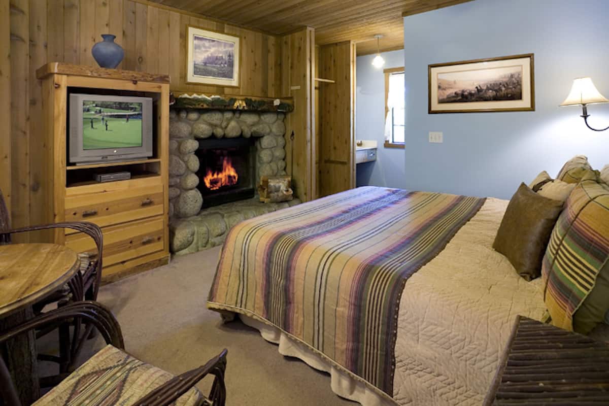 A cozy room with a stone fireplace, a television, a bed with striped bedding, and a dining area with a wooden table and chairs.