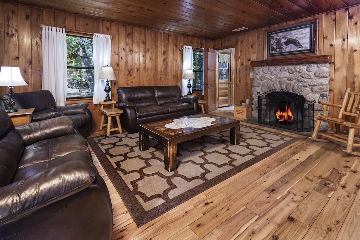A cozy living room with a stone fireplace, leather sofas, and a wooden floor.