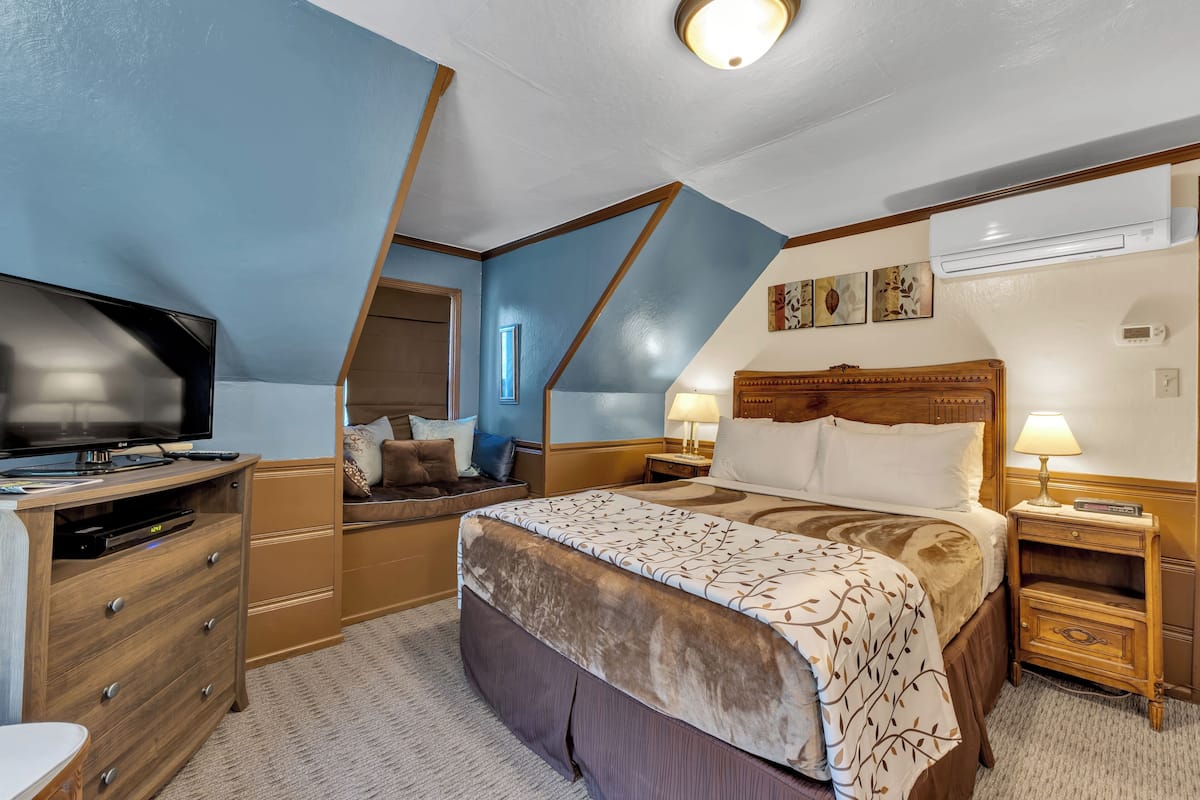 A bedroom with a bed, bedside tables, a TV, a dresser, and a ceiling light.