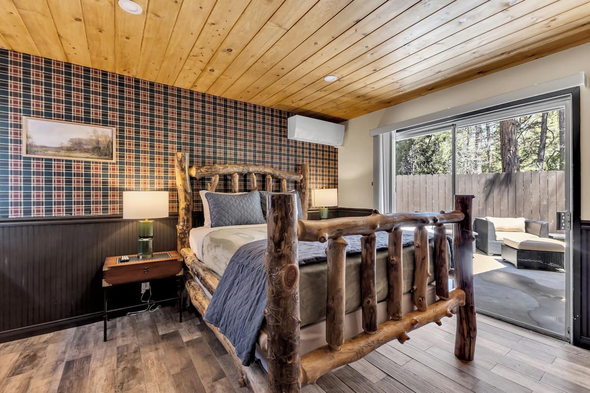 A bedroom with a wooden bed, a plaid-patterned wall, a window, and a view of the outdoors.