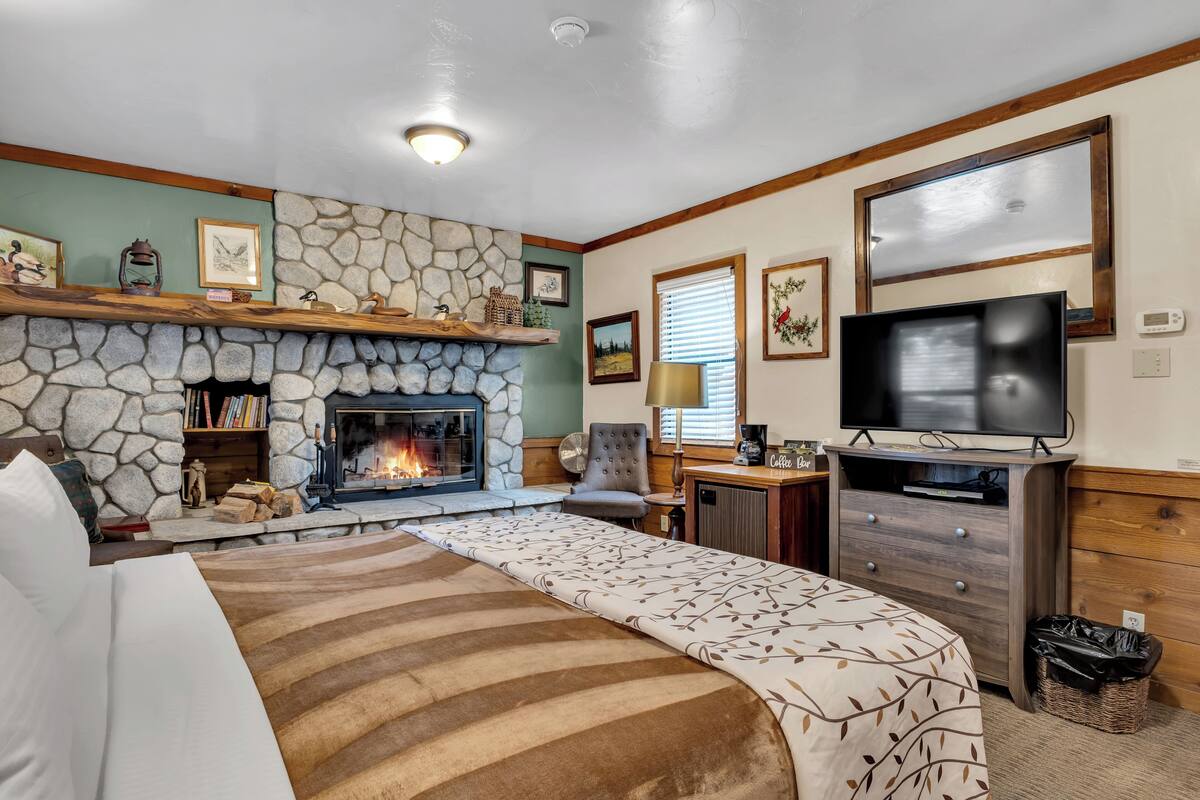 A cozy room with a stone fireplace, a bed with a patterned bedspread, a television, and a wooden dresser.