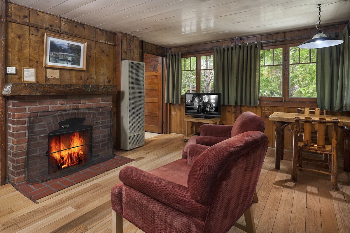 A cozy cabin interior with a brick fireplace, a television, and a dining area.