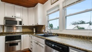 A modern kitchen with white cabinets, stainless steel appliances, granite countertops, and a window providing a view of the outdoors.
