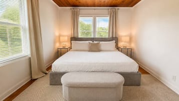 Une chambre à coucher avec un lit double, deux tables de chevet, un banc et une fenêtre avec des rideaux.