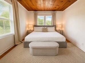 Une chambre à coucher avec un lit double, deux tables de chevet, un banc et une fenêtre avec des rideaux.