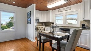A kitchen with white cabinets, a dining table with chairs, and a view of the outside.