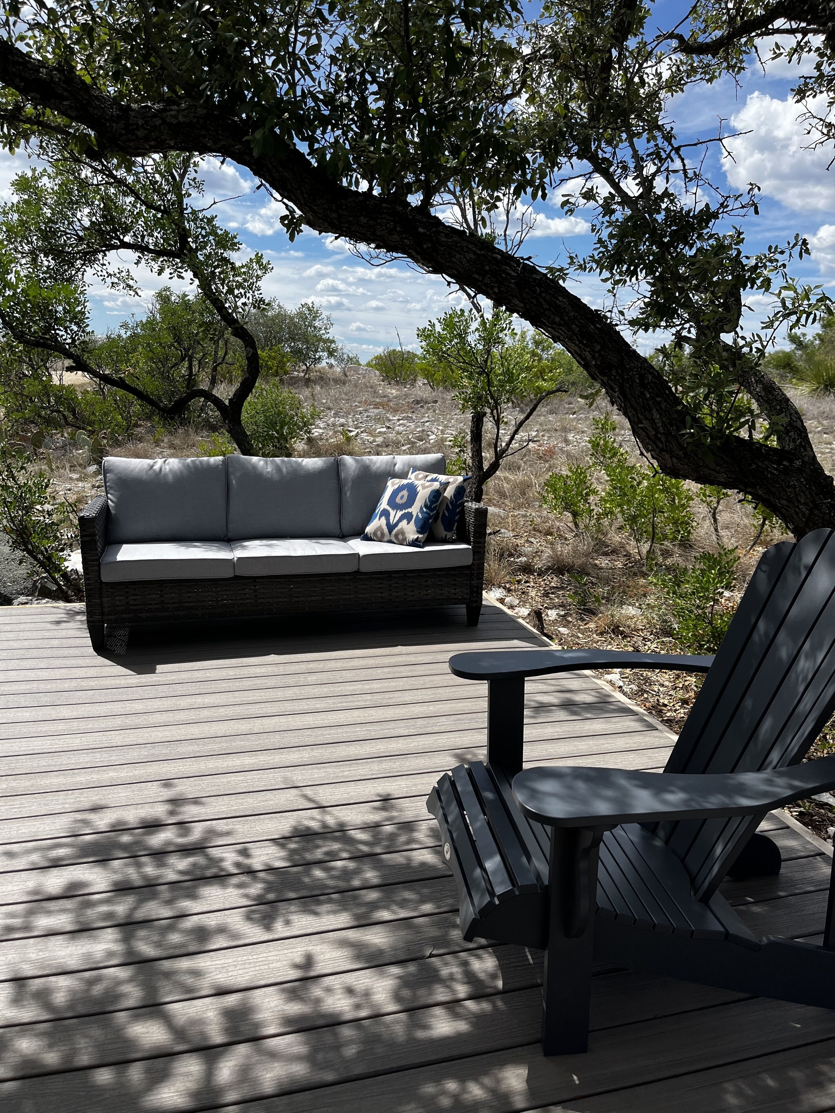 A wooden deck with a gray sofa and a black chair.