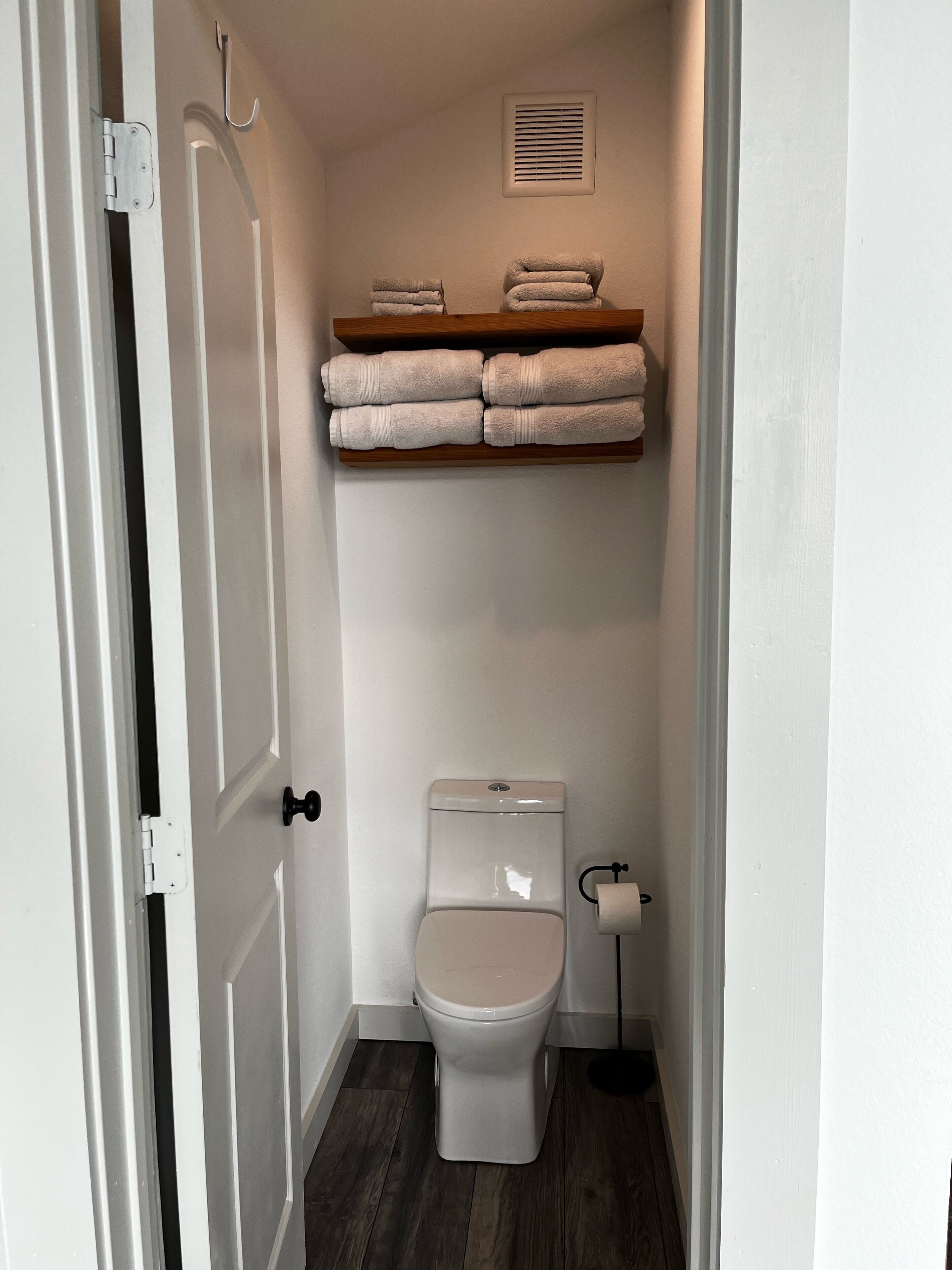 Un baño pequeño con inodoro, un perchero con toallas dobladas y un respiradero en la pared.