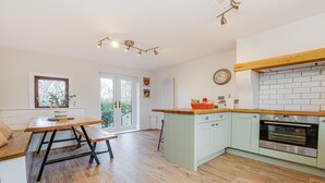 A modern kitchen with a wooden table, a built-in oven, and a window with a view of greenery. - Canal side cottage with hot tub, sky tv and log fire (Lathom)