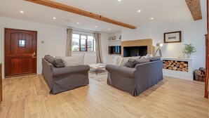 A living room with two grey sofas, a wooden floor, a TV, and a fireplace. - Canal side cottage with hot tub, sky tv and log fire (Lathom)