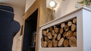A room with a fireplace, a stack of firewood, and a chair. - Canal side cottage with hot tub, sky tv and log fire (Lathom)