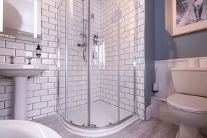 Ein modernes Badezimmer mit einer Duschkabine, weißen Fliesen im U-Bahn-Stil, einem weißen Waschbecken und einer Toilette.